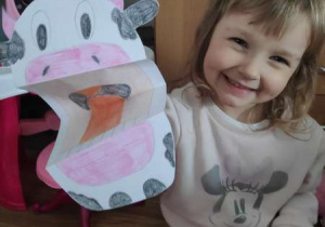 Ta sama dziewczynka trzyma krowę z papieru z otwartą mordką – krowa 3D